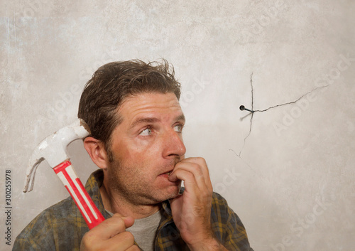 Photography funny portrait of man holding hammer after driving a nail for hanging a frame bu