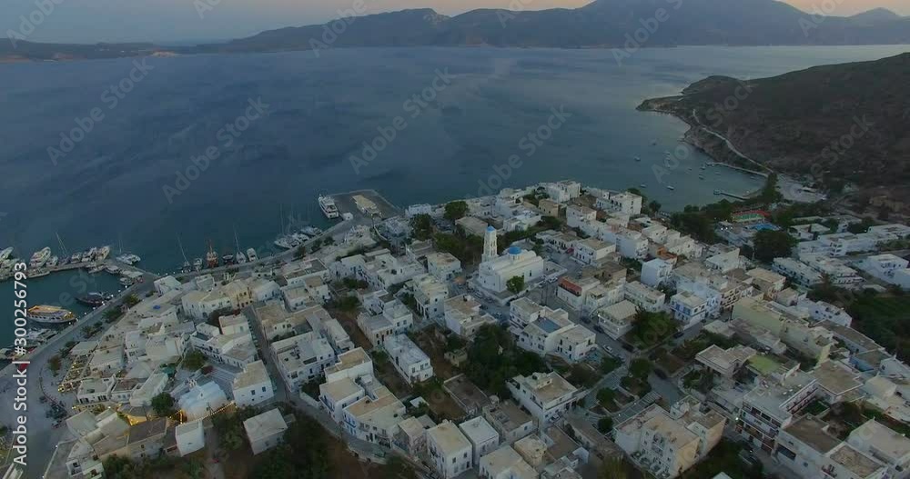Aerial pullback of an island village and church with blue roofs in the summertime in Greece. Daytime exterior at orange sunset vacation with Aegean Sea in the background. Milos Greece. Aerial pullback of an island village and church with blue roofs in the summertime in Greece. Daytime exterior at orange sunset vacation with Aegean Sea in the background. Milos Greece.