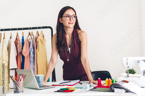Smiling asia woman fashion designer working with laptop computer at workshop studio