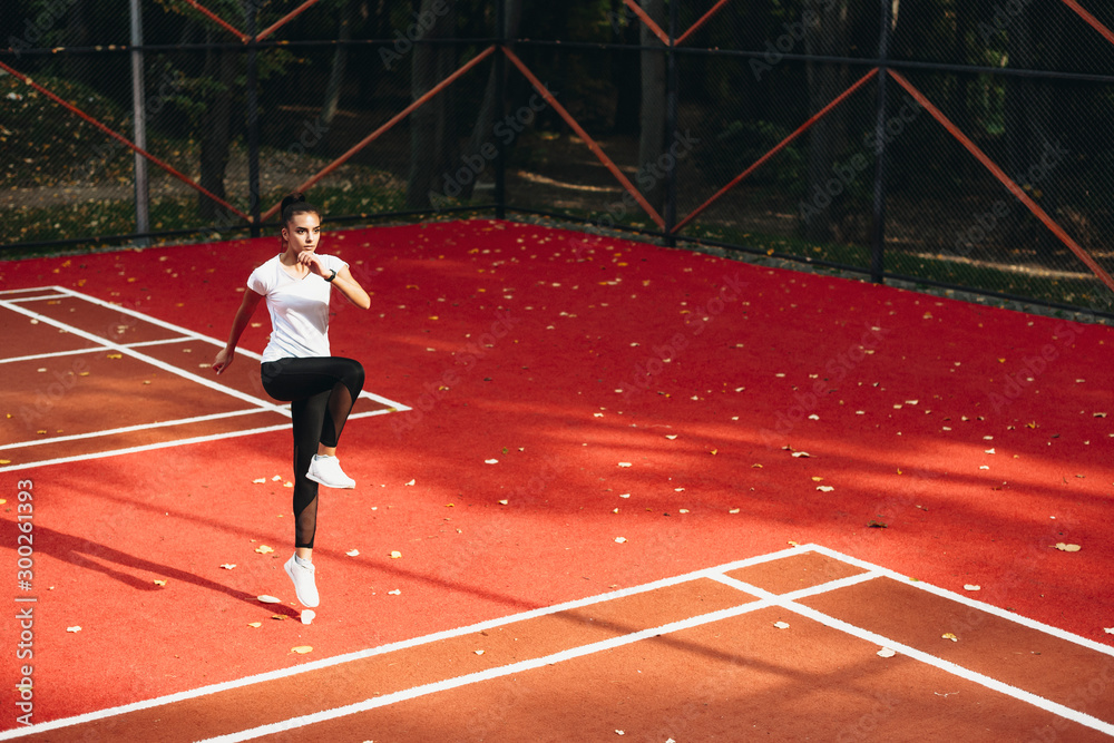 Fototapeta premium Sport woman jumping and stretching. Young female doing morning exercises in a sport park.