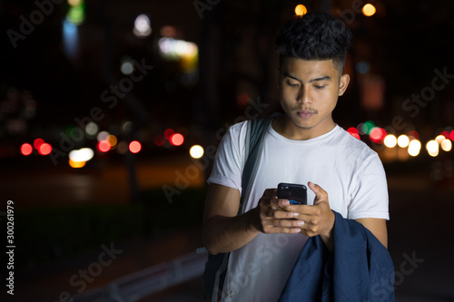 Young Asian man using phone in the city streets at night