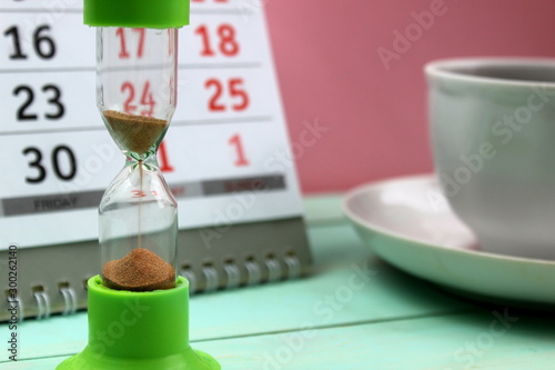 hourglass stand on the background of a calendar and a cup of coffee