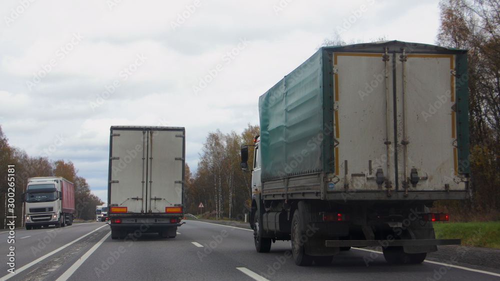 Naklejka premium Trucks overtaking, vehicles moving on autumn asphalt highway, road rules, traffic, lorry rear view