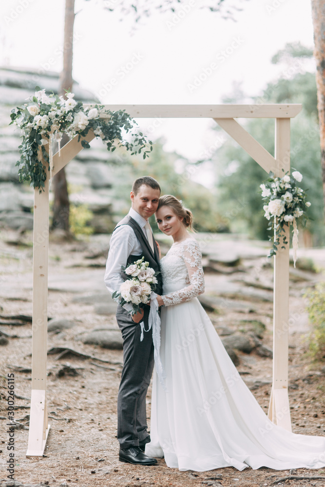 Fototapeta premium Beautiful couple at sunset in the Park. Wedding ceremony with arch in the forest.