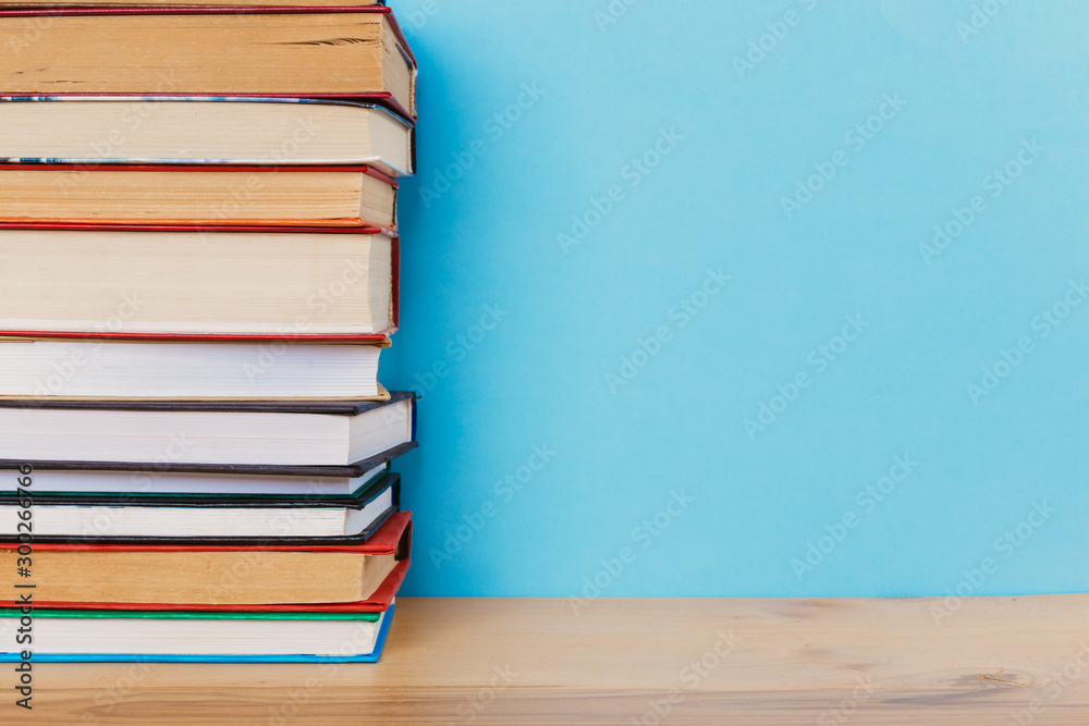 A simple composition of many hardback books, raw books on a wooden table and a bright blue background A simple composition of many hardback books, raw books on a wooden table and a bright blue background