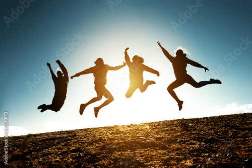 Four jumping silhouettes friends against sun photo