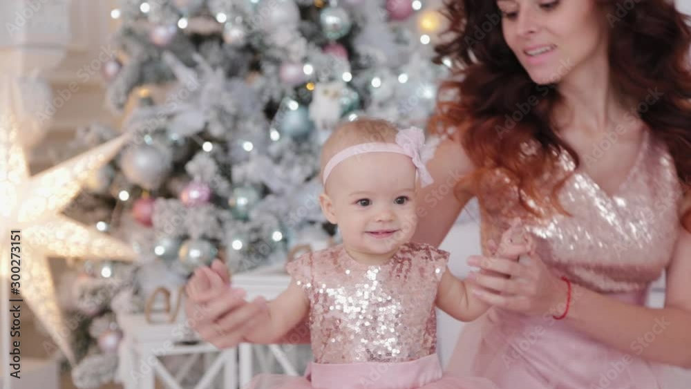 Beautiful mother with a one-year-old daughter in beautiful dresses and New Year's decor. New Year 2020. Beautiful mother with a one-year-old daughter in beautiful dresses and New Year's decor. New Year 2020.