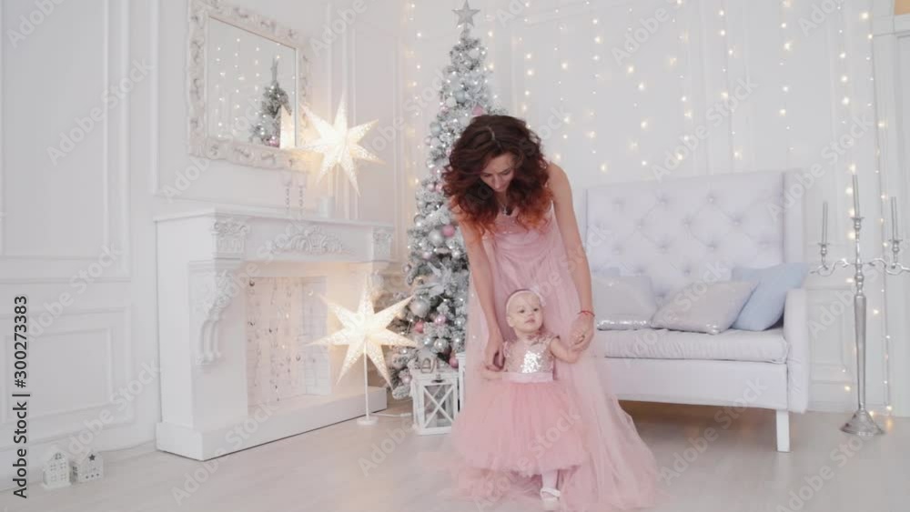 Beautiful mother with a one-year-old daughter in beautiful dresses and New Year's decor. New Year 2020.
