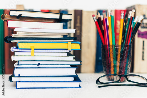 Notebooks piles, stack of books education back to school background, textbooks, glasses and pencils in holder with copy space for text.