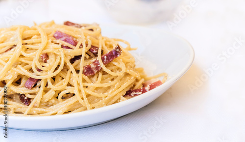 Pasta carbonara spaghetti with ham, bacon and fresh parmesan on the white plate in restaurant in Catania, Sicily, Italy.