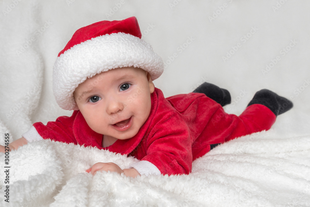 Little baby in Santa Claus costume is lying on white blanket Little baby in Santa Claus costume is lying on white blanket