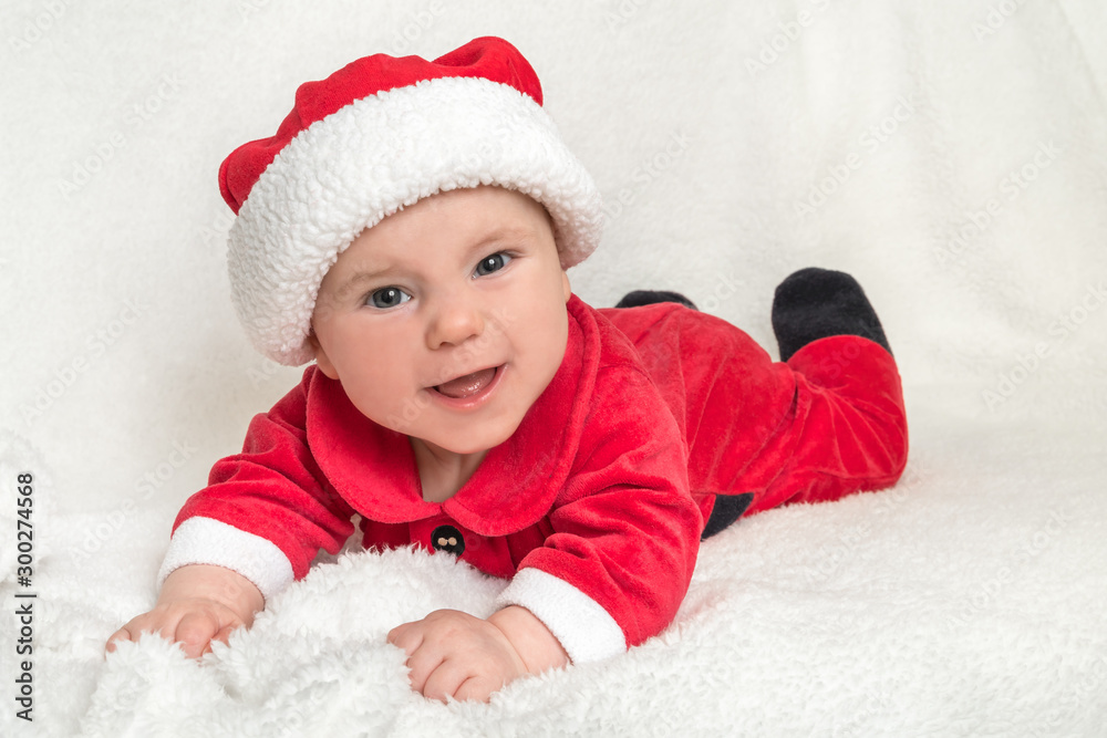 Little baby in Santa Claus costume is lying on white blanket Little baby in Santa Claus costume is lying on white blanket