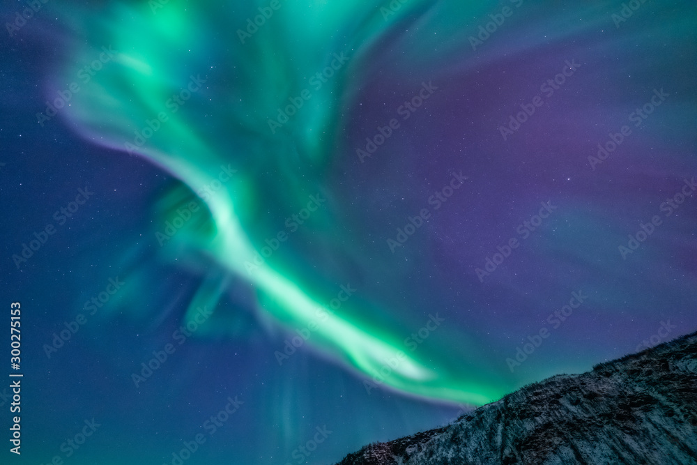 Aurora borealis in the sky above mountain with snow. Northern ligths, green purple and blue colors. Tromso, Norway.