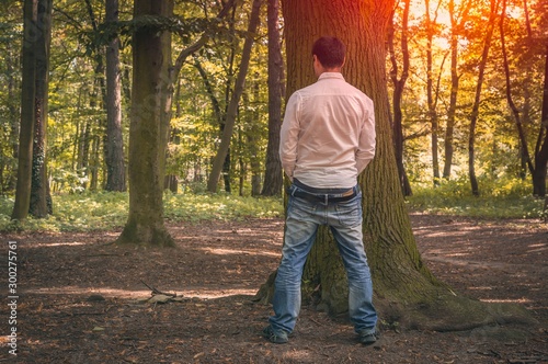 Standing man peeing near big tree in autumn forest