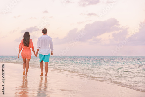 Luxury romantic Caribbean getaway for lovers walking on sunset beach stroll for honeymoon destination. Woman and man couple holding hands going away.