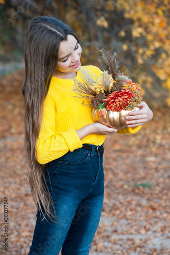 Beautiful girl walking outdoors in autumn. Smiling with  bouquet of flowers in gold pumpkin outdoor. Decorative pumpkin at halloween for home decoration.