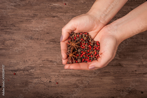 Hands holding the mixture of black and rose pepper in the shape of heart on the wooden background with the place for design mokup.