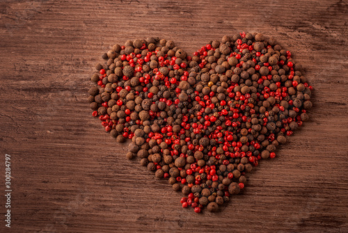 Dried black and rose pepper in the shape of heart on the wooden background.