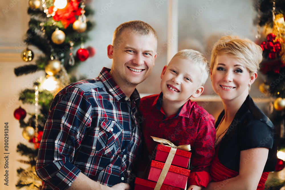 Portrait of cheerful beautiful caucasian family with red gift boxes smiling at camera against Christmas decoration. Family concept. Christmas time and New Year. Portrait of cheerful beautiful caucasian family with red gift boxes smiling at camera against Christmas decoration. Family concept. Christmas time and New Year.