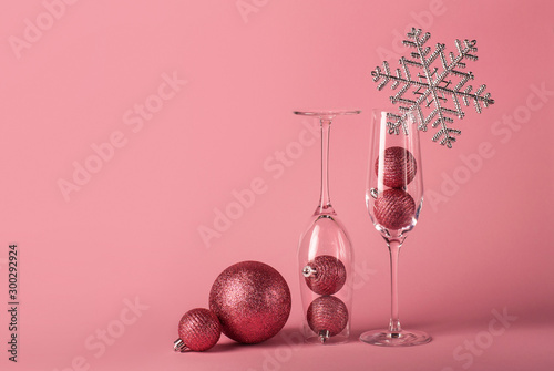 Two glasses for champagne with Christmas balls inside, decorated with silver snowflake on the pink background. The mockup for Christmas and  New Year