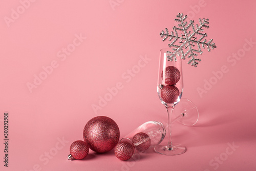 Two glasses for champagne with Christmas balls inside, decorated with silver snowflake on the pink background. The mockup for Christmas and  New Year