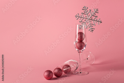Two glasses for champagne with Christmas balls inside, decorated with silver snowflake on the pink background. The mockup for Christmas and  New Year