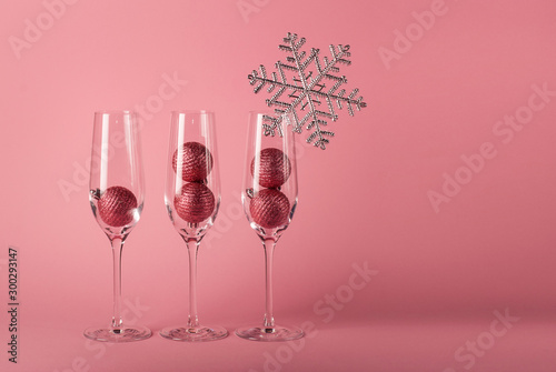 Three glasses for champagne with Christmas balls inside, decorated with silver snowflake on the pink background. The mockup for Christmas and  New Year