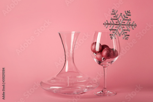 The wine glass with Christmas balls inside, decorated with silver snowflake on the pink background. The mockup for Christmas and  New Year. Wine decanter.