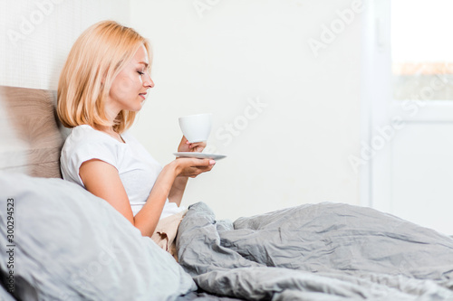 Woman sitting on bed drinking coffee