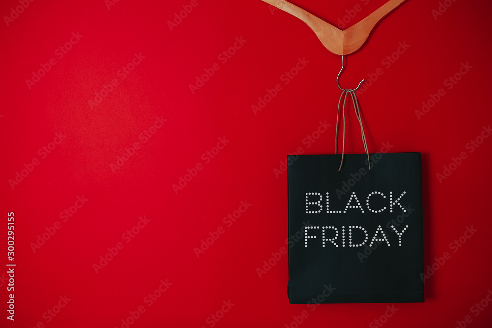 Black friday image with space for text. Bkack friday sale flat lay. Black friday bag. Hangers on the red background.