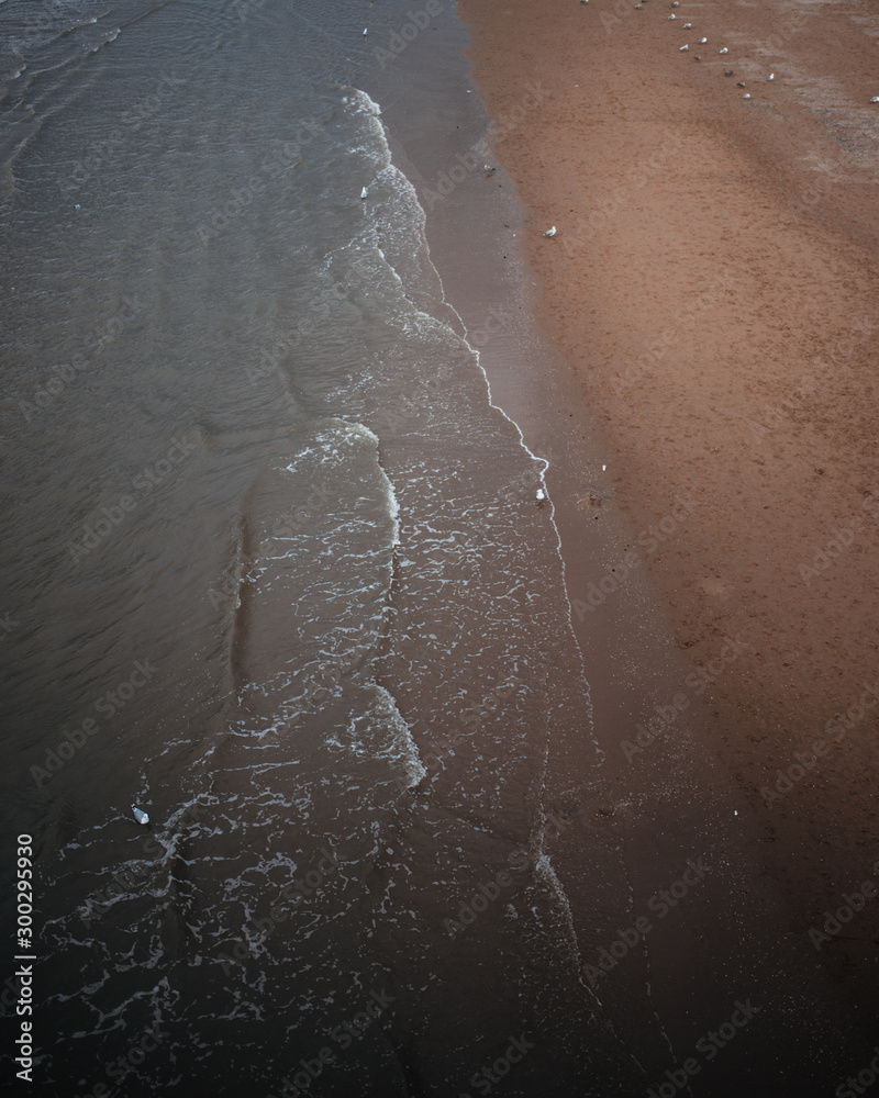 Fototapeta premium Waves crashing into a sandy beach, dark moody summer photo