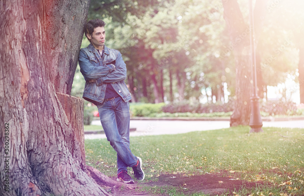 Naklejka premium A young man walks in the park at lunch time. A man is on a walk in the city. A student in the park.