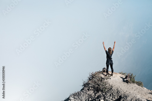 Young woman have fun on summit of active volcano. Stand on high cliff above crater acid lake with poisonous fume. Popular travel destination, adventure hike on family vacation in Bali, Java, Indonesia