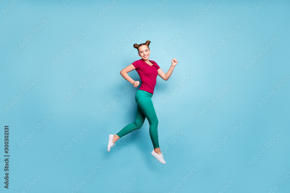 Full length body size photo of cheerful positive side profile girl wearing red t-shirt smiling toothily running for sales jumping up in trousers green isolated pastel blue color background