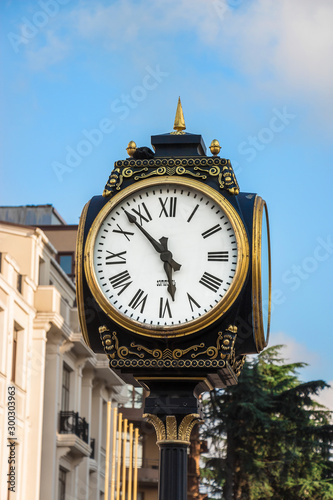 Old Street Clock In Europe. Clock Face With Roman Numerals And Arrows, Cast-iron Column And Gold Decorative Elements.