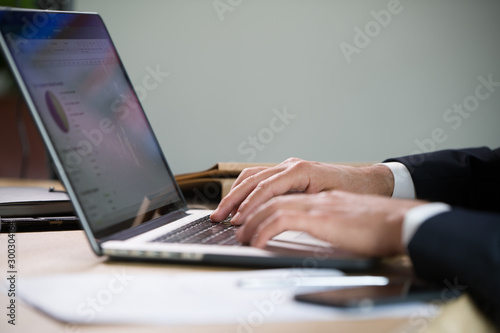 Close-up of male hands typing on a laptop in an office setting