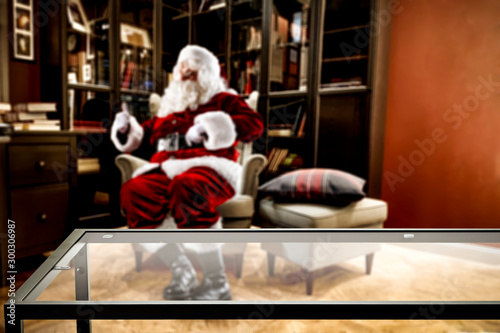 Santa Claus sitting in an armchair and resting in a living room after delivering presents. Comfortable and cozy place in home interior. Table top space for products and decorations or text.