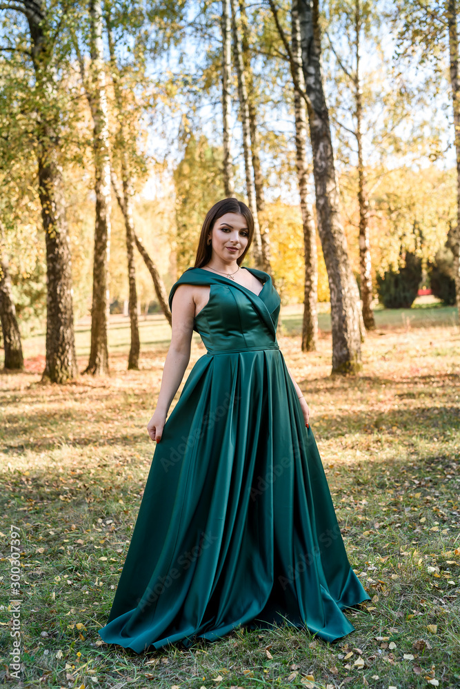 Young woman wearing fashionable green dress walking in autumn park.