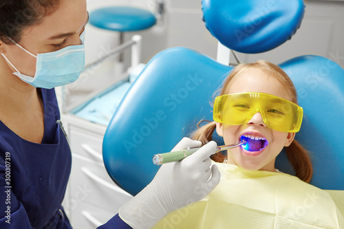 Process of drying the dental seal after treatment of the patient's tooth in pediatric dentistry. Little girl in dentist office.
