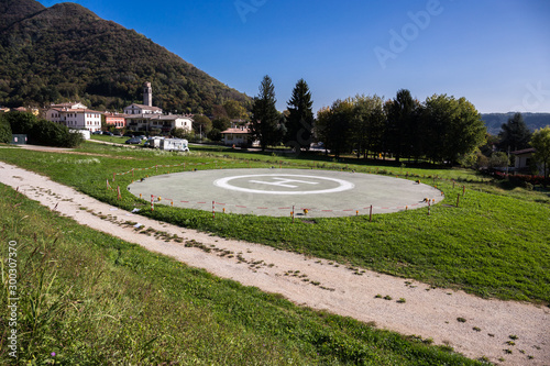 Foto Landing place for a helicopter on a field with village nad mountain in the backg