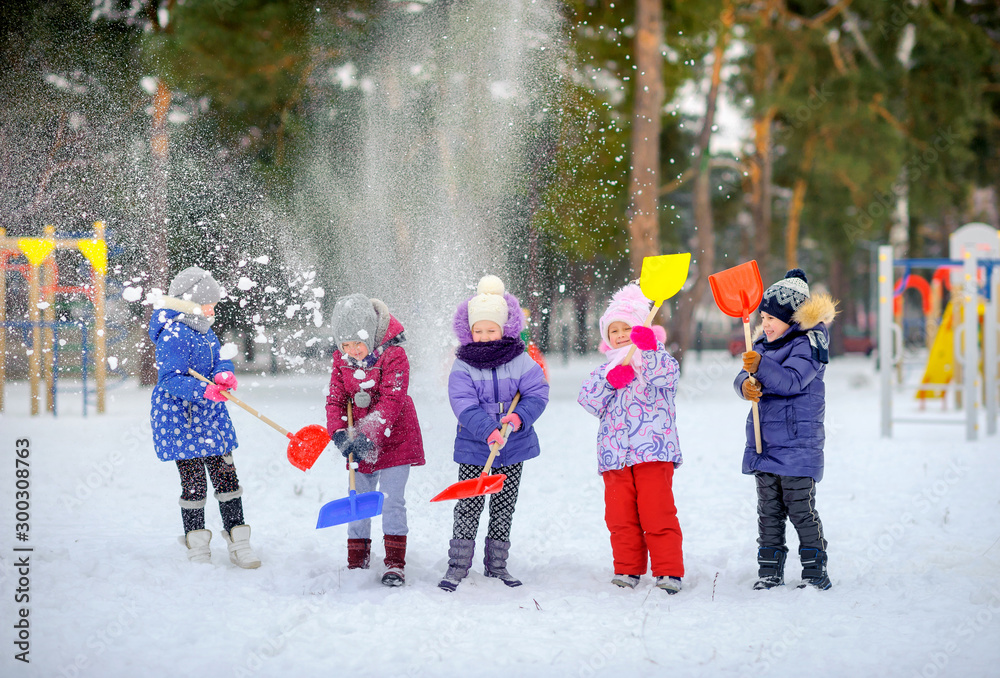 A group of children are playing and having fun on a winter playground. Friends throw snow with shovels and laugh. Winter fun. holidays