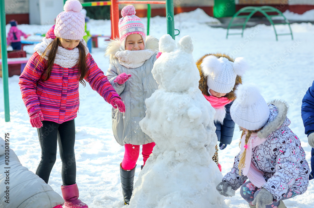 Friends make a snowman on a winter playground, children's games, Holidays
