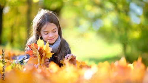 Cute girl lies in the park on the grass and collects autumn fallen leaves
