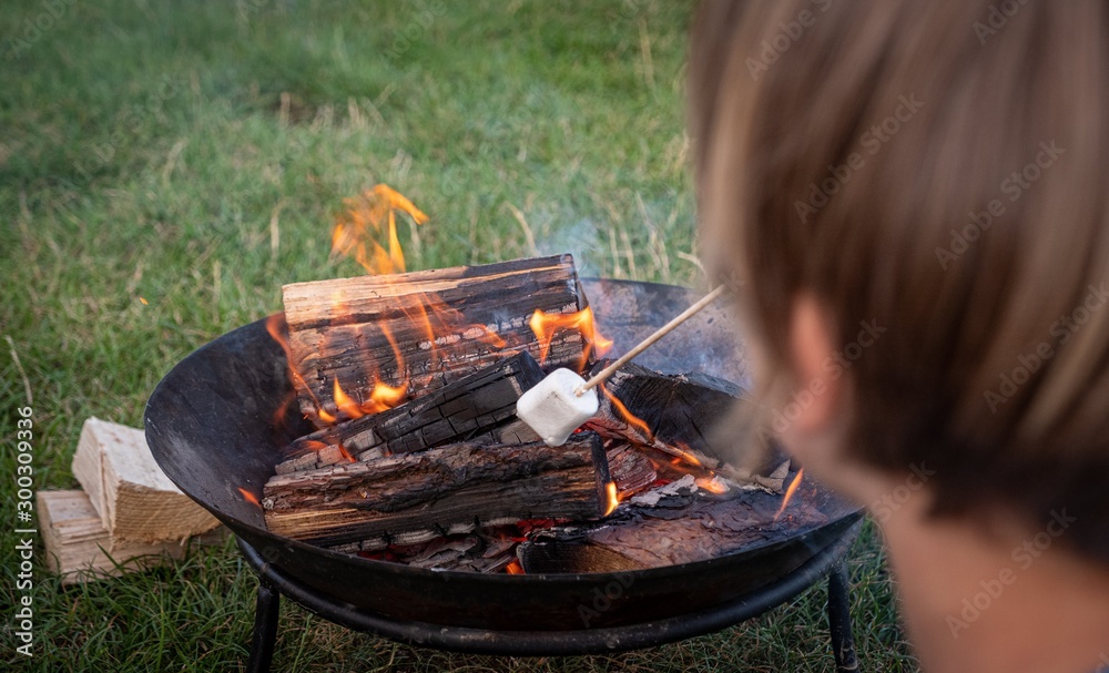 Fototapeta premium Happy young man and his son enjoying their weekend in natural environment while frying marshmellow on campfire