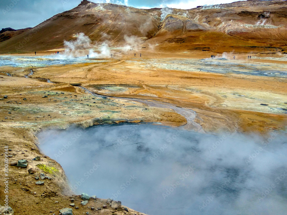 Iceland. Tourists walk around the turmal springs. Steam rises above the hot springs.