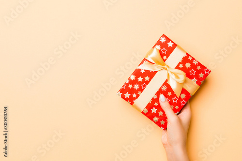 Flat lay of woman hands holding gift wrapped and decorated with bow on gold background with copy space. Christmas and holiday concept
