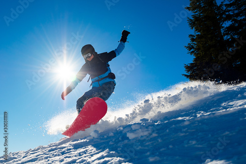 Snowboarder Riding Red Snowboard in Mountains at Sunny Day. Snowboarding and Winter Sports photo