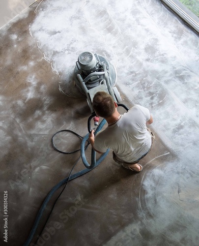 Construction worker in a family home living room that grind the concrete surface before applying epoxy flooring.Polyurethane and epoxy flooring.Concrete grinding. photo