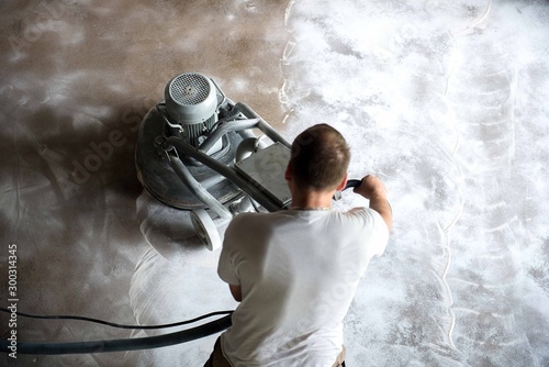 Construction worker in a family home living room that grind the concrete surface before applying epoxy flooring.Polyurethane and epoxy flooring.Concrete grinding. photo