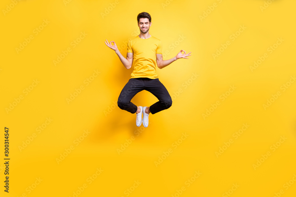Full body photo of handsome guy jumping high lotus position morning yoga training relaxing fingers together wear casual t-shirt black trousers isolated yellow color background
